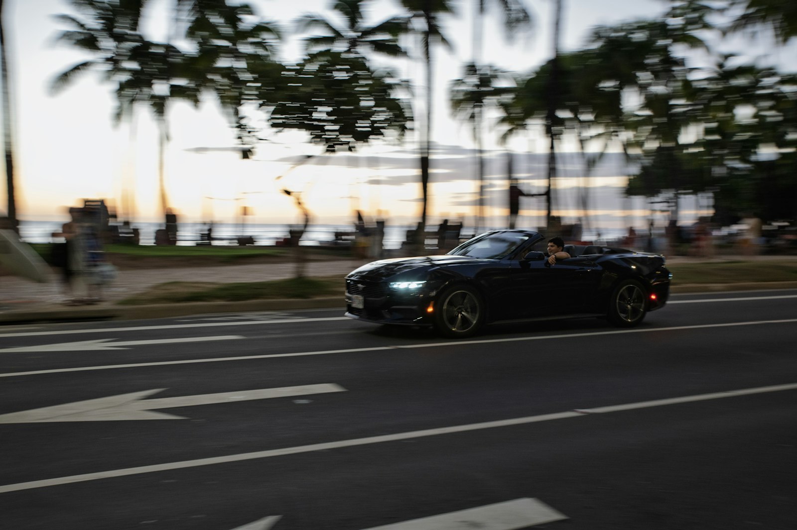 A convertible arriving along a coastal road at golden hour